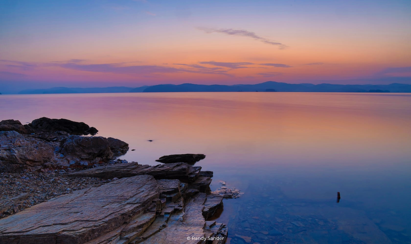 Sunset over a calm lake with rocky shoreline